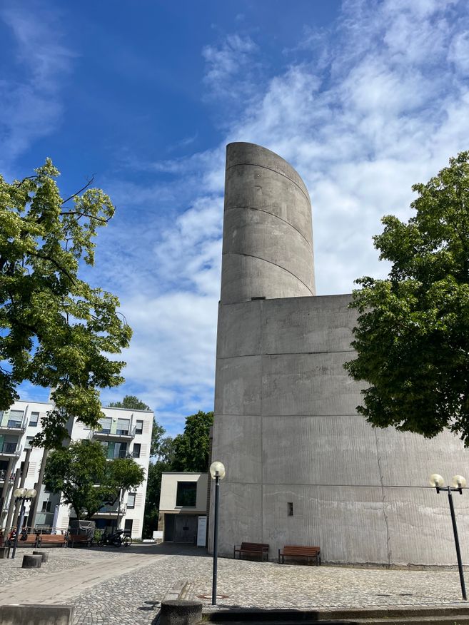 Blauer Himmel, Bäume und moderner Kirchturm aus Beton