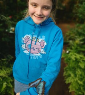 Ein großer blauer Schmetterling sitzt auf dem Arm eines KIndes. Das Kinder trägt einen blauen Pullover und lächelt in die Kamera
