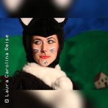 Person in einem Katzenkostüm mit bemaltem Gesicht vor einem grünen Hintergrund.