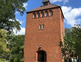 Backsteinturm mit Bäumen und blauem Himmel im Hintergrund.