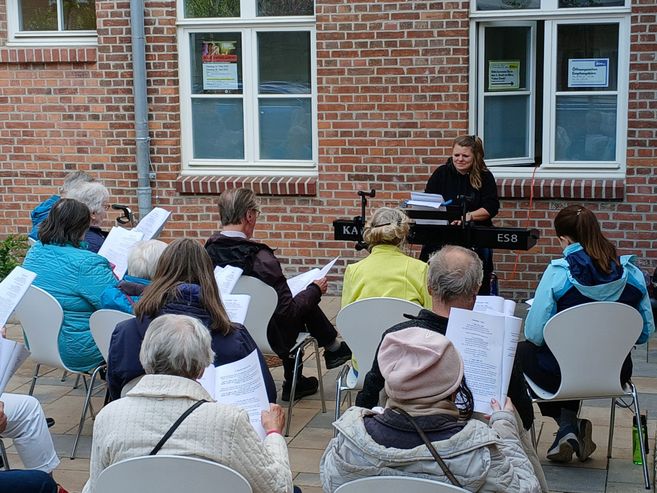 Menschen sitzen draußen vor dem Kulturzentrum und singen gemeinsam