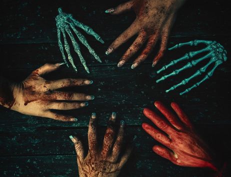 Mehrere blutverschmierte Hände und Skeletthände liegen auf dunklem Holz, gruselige Halloween-Szene.