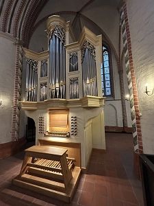 Eine große Kirchenorgel mit mehreren Pfeifen und einem hölzernen Spieltisch in einem Kirchenraum mit Backsteinwänden.