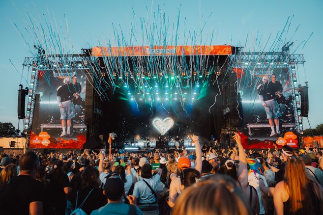 Menschenmenge vor einer großen Festivalbühne mit Lichteffekten und Konfetti.