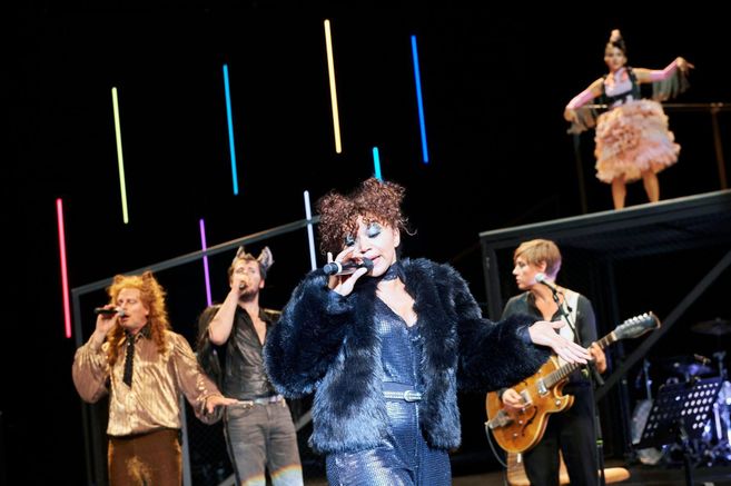 Sänger und Musiker auf einer Bühne mit bunten Lichtern im Hintergrund.