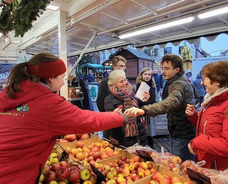 Menschen kaufen Äpfel an einem Marktstand mit Weihnachtsdekoration.