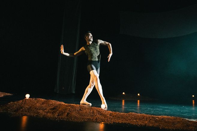 Ausschnitt aus der Tanzproduktion »Choreographing Story »Rama House«« von Chen Wu-kang und Pichet Klunchun. Eine performende Person bewegt sich in einer Ballett-Pose über die Bühne. Vor ihr ist ein kleiner erdartiger Hügel aufgescharrt.