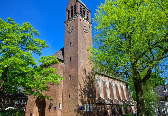 Backsteinkirche mit Turm und grünen Bäumen im Vordergrund.