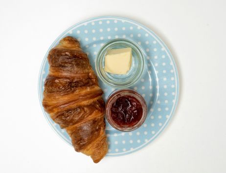 Ein Croissant mit Butter und Marmelade auf einem blauen Teller mit weißen Punkten.