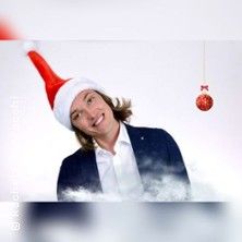Person mit Weihnachtsmütze und Anzug vor weißem Hintergrund mit Weihnachtskugel.