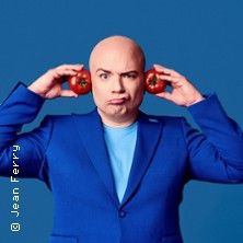 Ein Mann in einem blauen Anzug hält Tomaten an seine Ohren vor einem blauen Hintergrund.