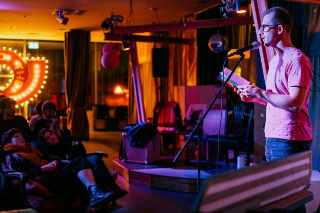 Ein Poetry Slammer steht auf der Bühne vor Publikum in gemütlichem Setting