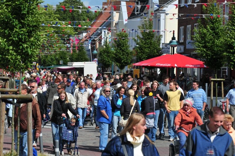 Menschenmenge auf einem belebten Straßenflohmarkt mit bunten Wimpeln und Sonnenschirmen.