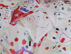 Bunte, handbemalte Drachen aus Papier mit verschiedenen Gesichtern und Mustern auf einem Tisch.