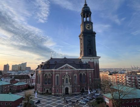 Die Kirche St. Michaelis in Hamburg bei Sonnenuntergang, mit der Elbphilharmonie im Hintergrund.