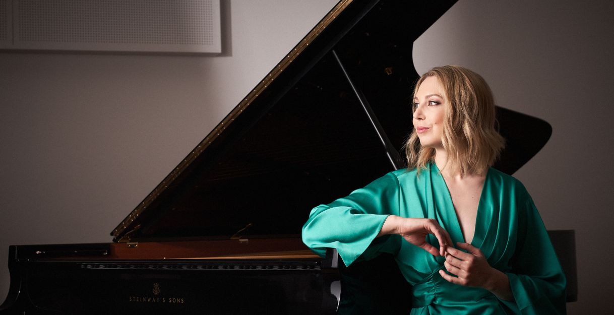 Eine Frau in einem grünen Kleid sitzt neben einem Flügel.