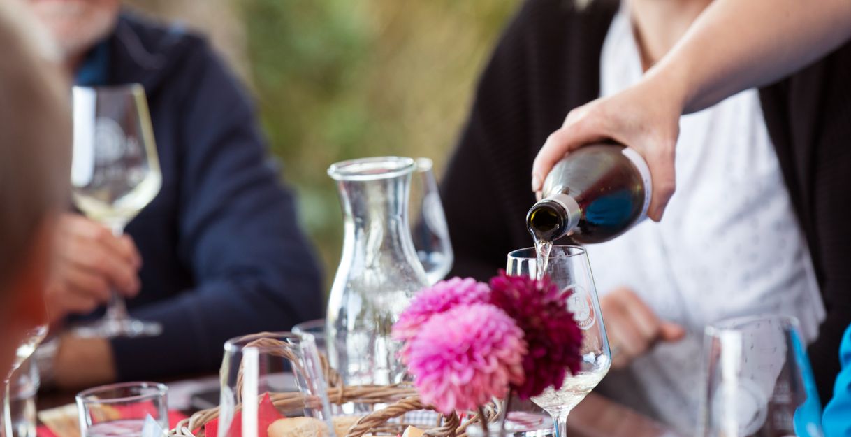 Eine Person schenkt Weißwein in ein Glas bei einem Tisch mit Blumen und Weingläsern.