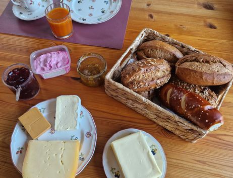 Frühstückstisch mit Brötchen, Käse, Marmelade und Getränken.