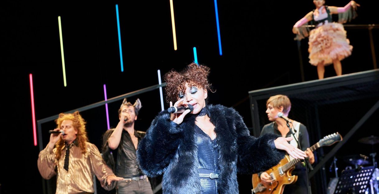 Sänger und Musiker auf einer Bühne mit bunten Lichtern im Hintergrund.