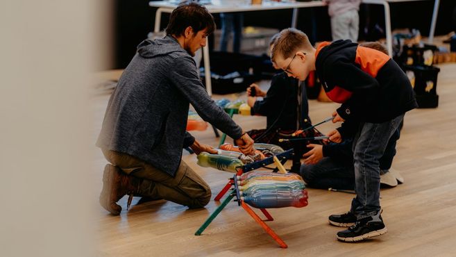 Ein Mann und ein Junge spielen auf bunten Trommeln aus recycelten Materialien.