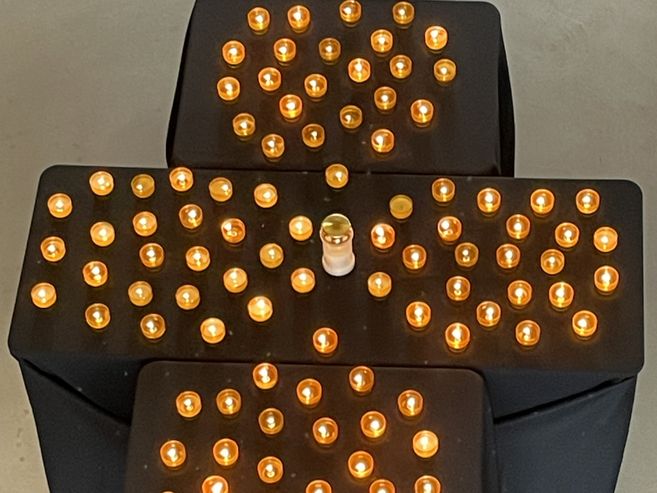 Kerzen in Form eines Kreuzes auf schwarzen Tischen angeordnet.