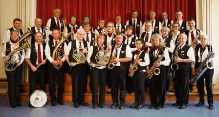 Eine Gruppe von Musikern in Uniformen mit Blasinstrumenten vor einem roten Vorhang.