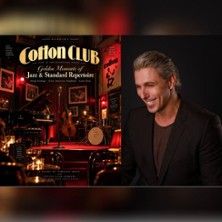 Mann vor einem beleuchteten Jazzclub-Interieur mit Bühne, Instrumenten und dem Schriftzug „Cotton Club“; links ein historisches Clubmotiv, rechts ein lächelnder Mann im Vordergrund.