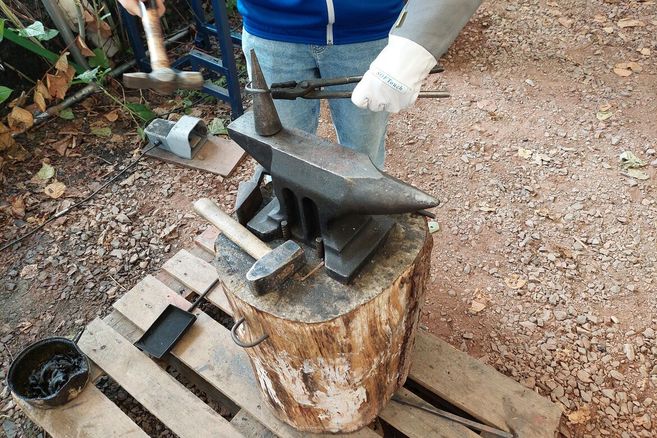 Eine Person schmiedet Metall auf einem Amboss im Freien.