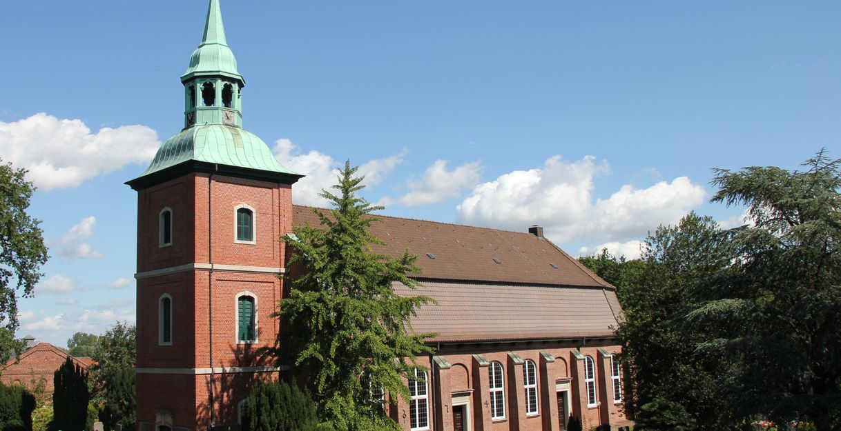 St. Pankratiuskirche in Ochsenwerder mit rotem Backsteinturm und grünem Dach vor blauem Himmel.