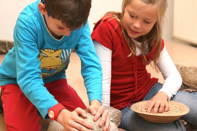 Zwei Kinder mahlen Getreide mit Steinen.