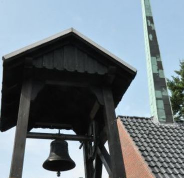 Das Christophorushaus in Schnelsen mit Glockenturm, Dach und einem hohen, gemusterten Schornstein vor blauem Himmel.