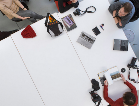 Menschen sitzen um einen Tisch mit Kameras und Fotobüchern.