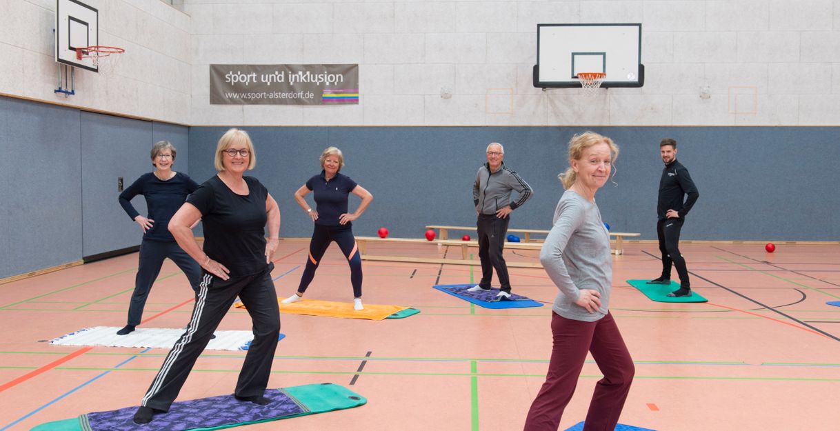 Sechs Personen posieren auf Yogamatten in einer Sporthalle.