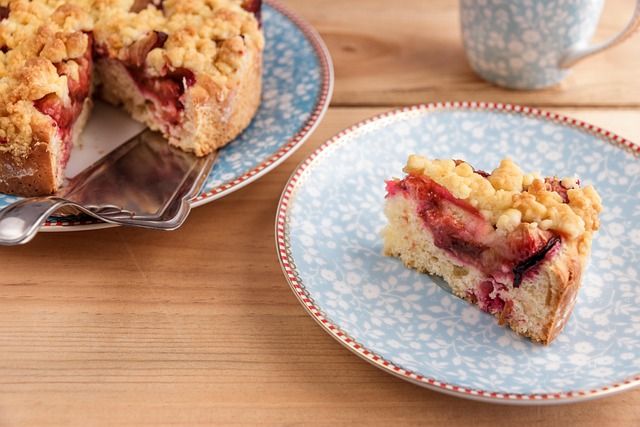 Ein Stück Pflaumenkuchen mit Streuseln auf einem blauen Teller, daneben eine Kaffeetasse.