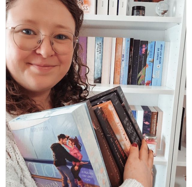 Person hält Bücher vor einem Bücherregal.