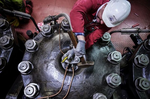 Ein Arbeiter in roter Kleidung und Schutzhelm bearbeitet eine große Metallmaschine mit einem Hammer.