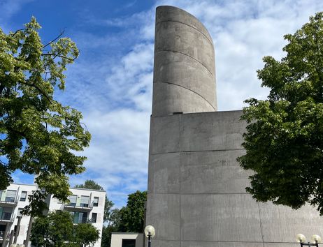 Blauer Himmel, Bäume und moderner Kirchturm aus Beton