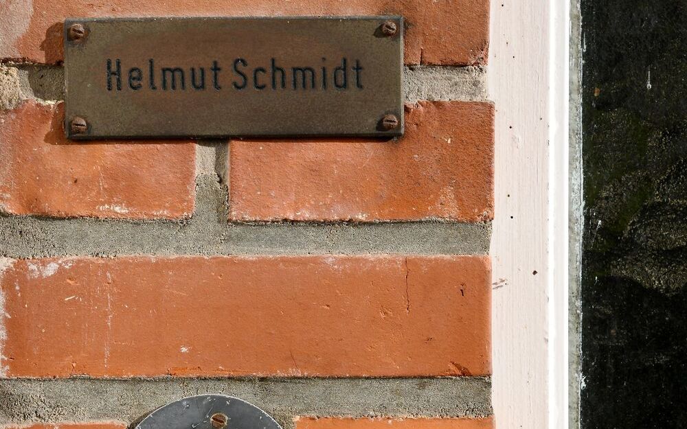 Foto eines kleinen Ausschnittes einer Hauswand aus Backstein, in die eine runde Klingel mit Klingeknopf eingelassen sowie ein Metalschild befestigt ist. Auf dem Schild steht "Helmut Schmidt".