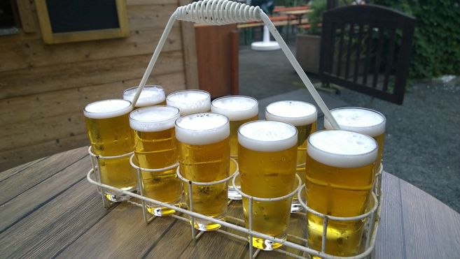 Ein Träger mit mehreren kleinen Biergläsern auf einem Holztisch im Freien.