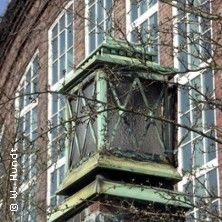 Nahaufnahme einer alten Laterne vor einem Backsteingebäude mit großen Fenstern.