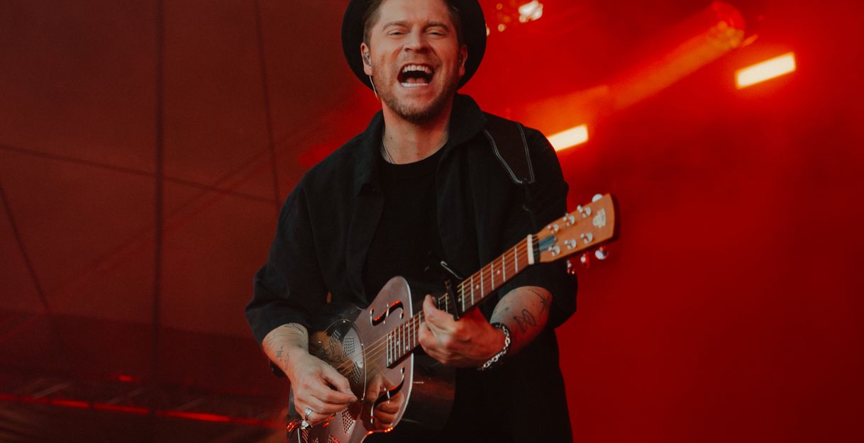 Ein Musiker spielt auf einer Gitarre auf einer Bühne mit rotem Licht.