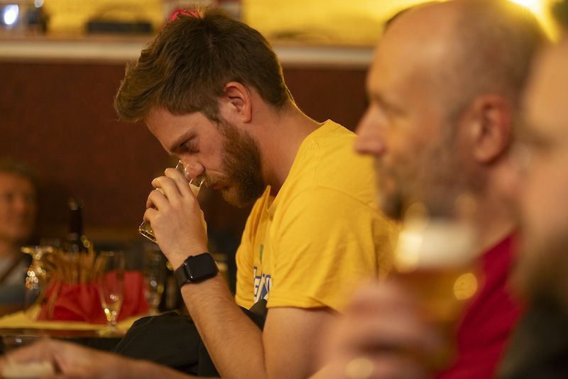 Mann in gelbem T-Shirt riecht an einem Bierglas in einer Bar.