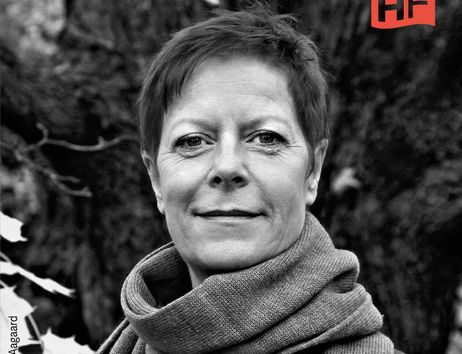 Schwarz-weiß Porträt einer Person mit kurzem Haar und Schal vor einem Baum.