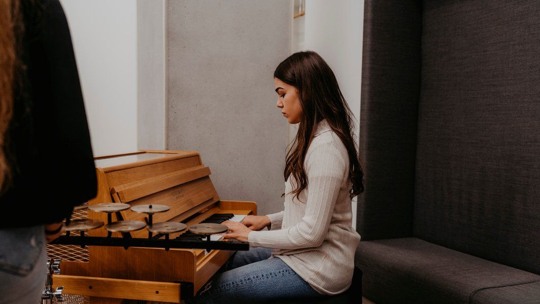 Eine Frau spielt auf einem Klavier mit kleinen Becken darauf in einem modernen Raum.