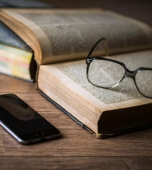 Smartphone, Brille und Buch auf einem Holztisch