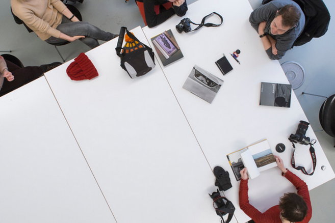 Menschen sitzen um einen Tisch mit Kameras und Fotobüchern.