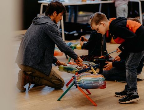 Ein Mann und ein Junge spielen auf bunten Trommeln aus recycelten Materialien.