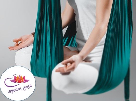 Person in weißer Kleidung praktiziert Aerial Yoga in einem türkisfarbenen Tuch.