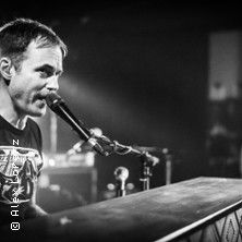 Schwarz-weiß-Foto eines Mannes, der an einem Klavier sitzt und in ein Mikrofon singt.