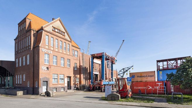 Backsteingebäude mit Containern und Kran im Hafenbereich.